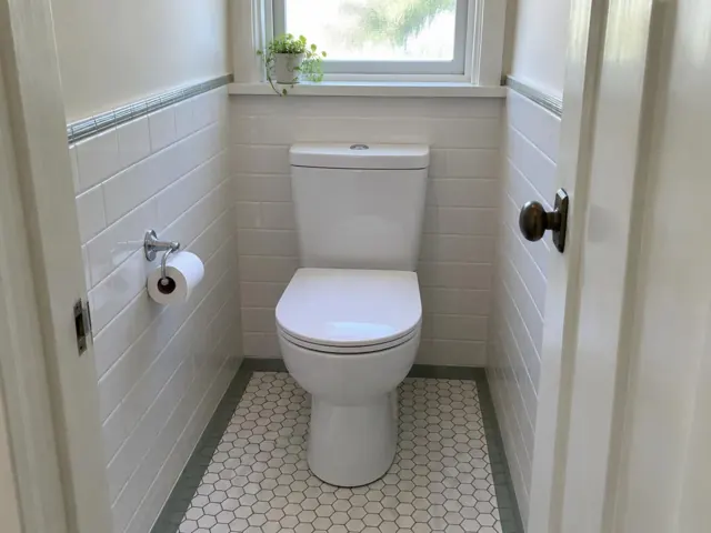 Clean white toilet in a small tiled bathroom with window light in Willoughby