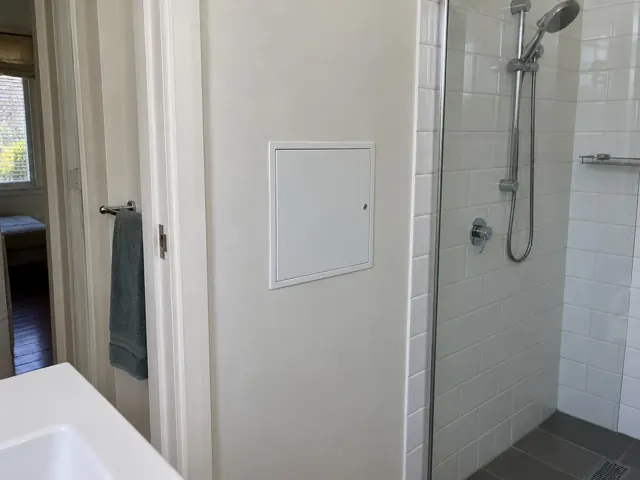 Bathroom wall with a small access panel beside a tiled shower and doorway in Naremburn